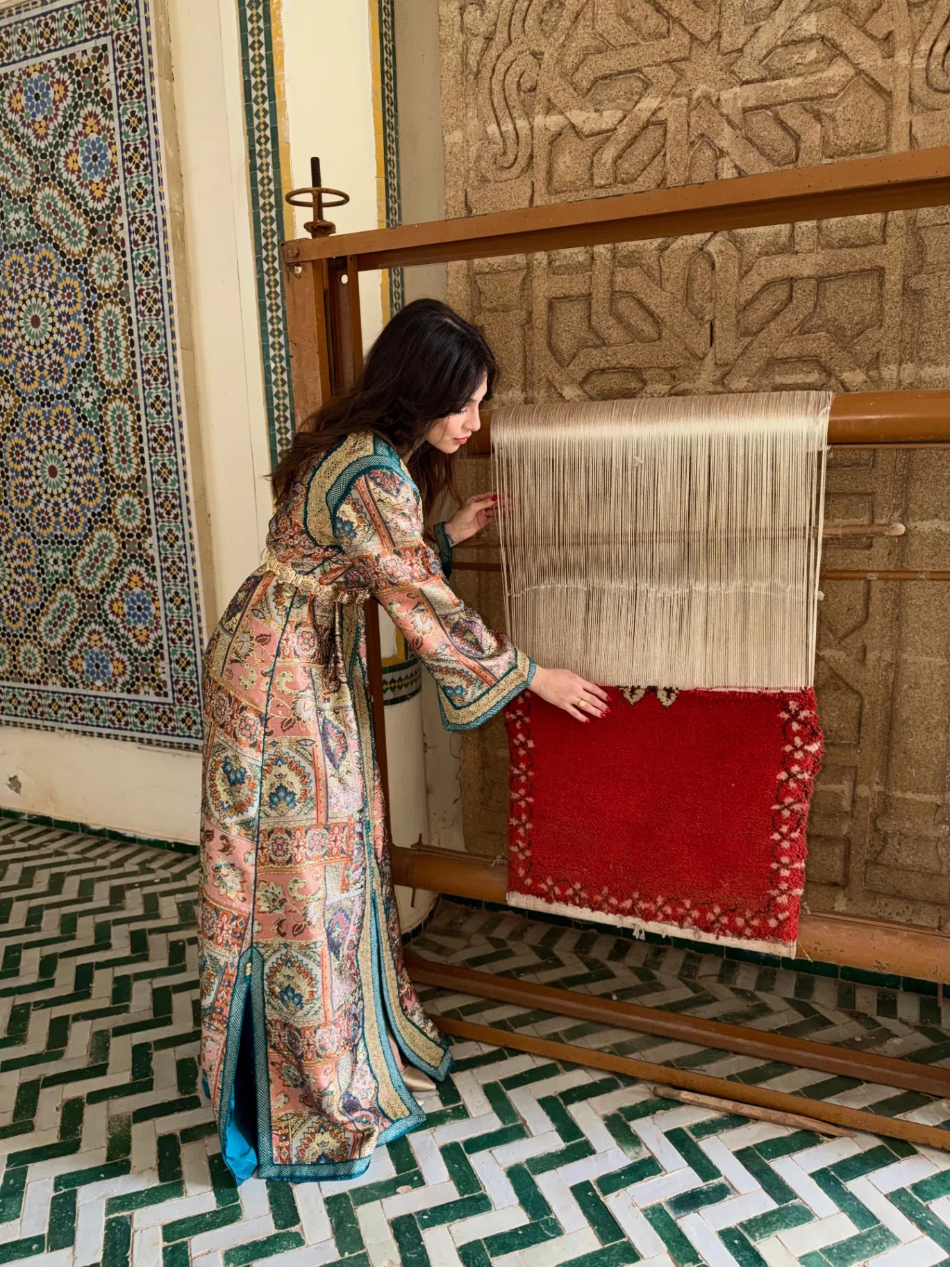Caftan brocart ocre à motifs de tapisserie, devant un métier à tisser